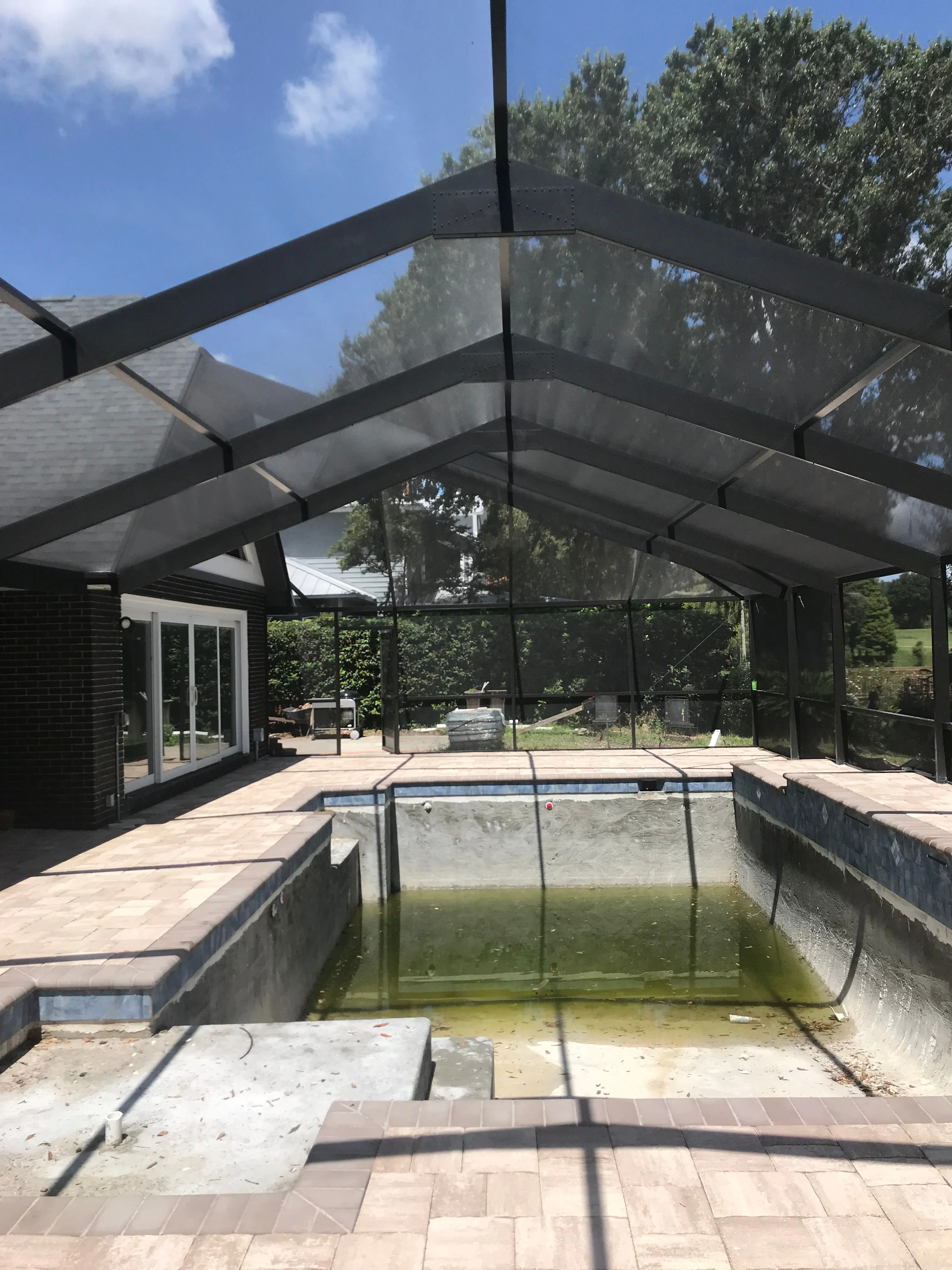 Outdoor construction workspace with aluminum framing materials, tools, and equipment ready for patio and screen enclosure projects.