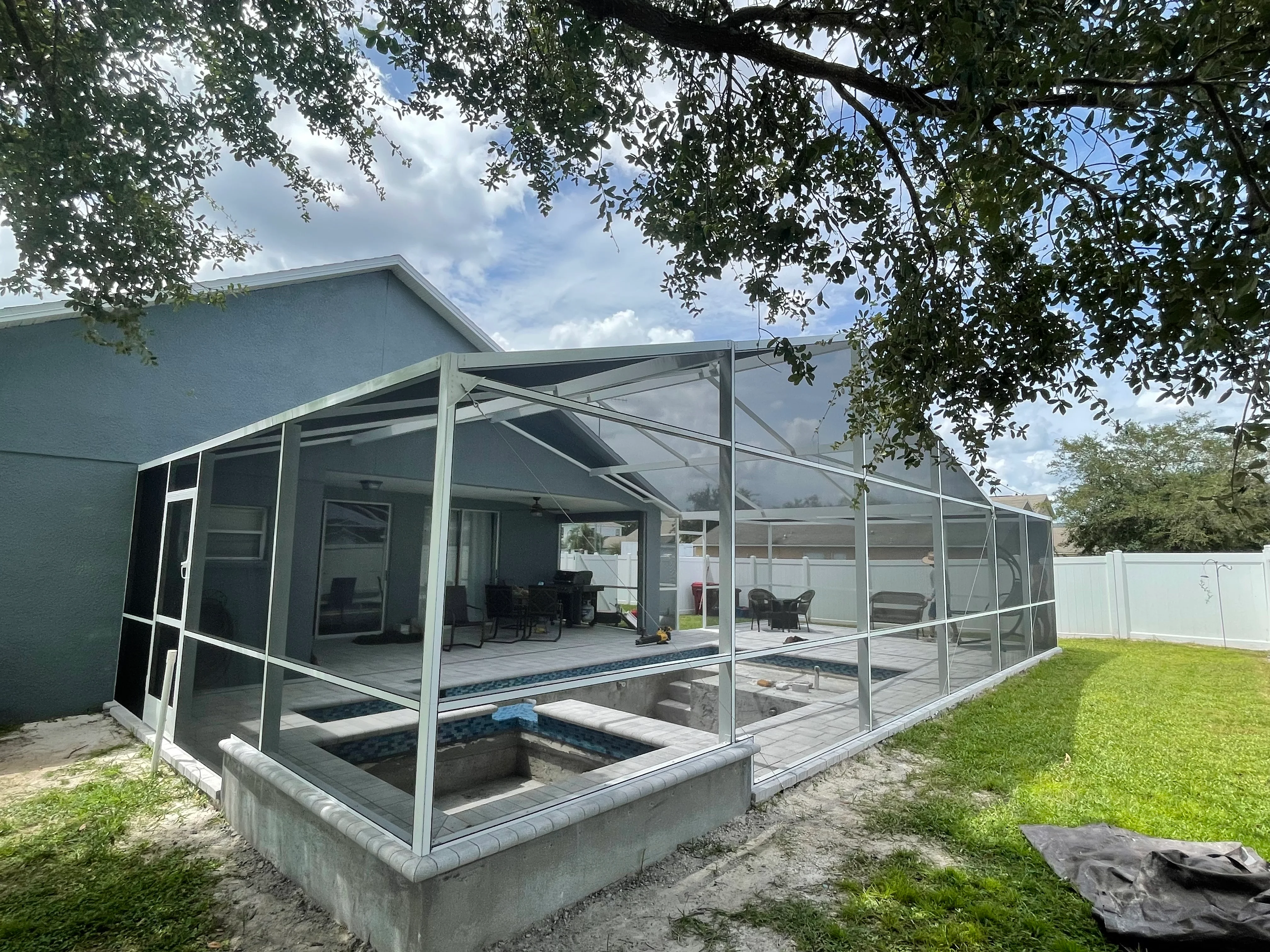 Aluminum screened patio with glass panels, gable roof, and concrete pool deck foundation
