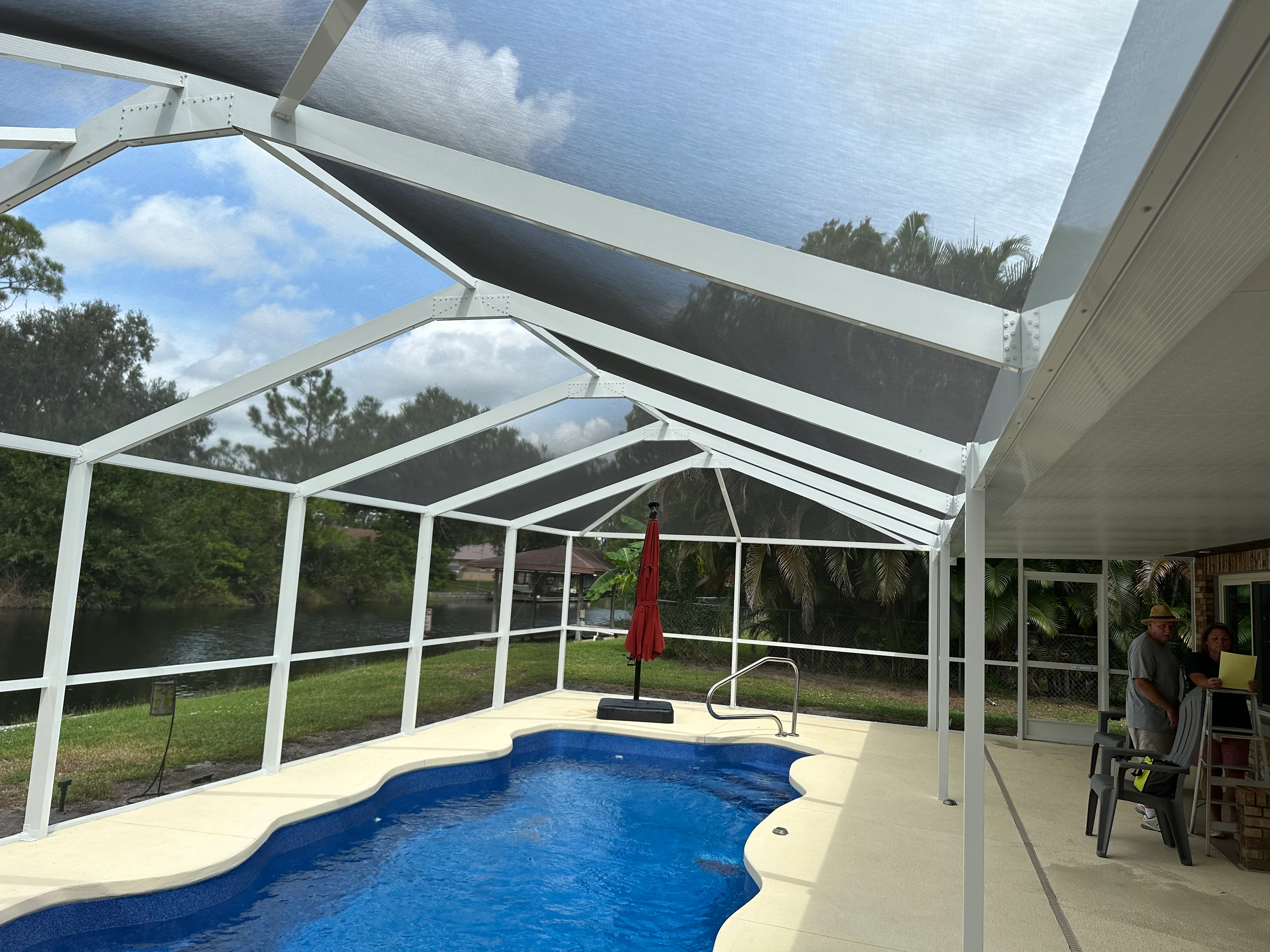 White aluminum pool enclosure with retractable shade panels, screening, and concrete deck beside blue pool