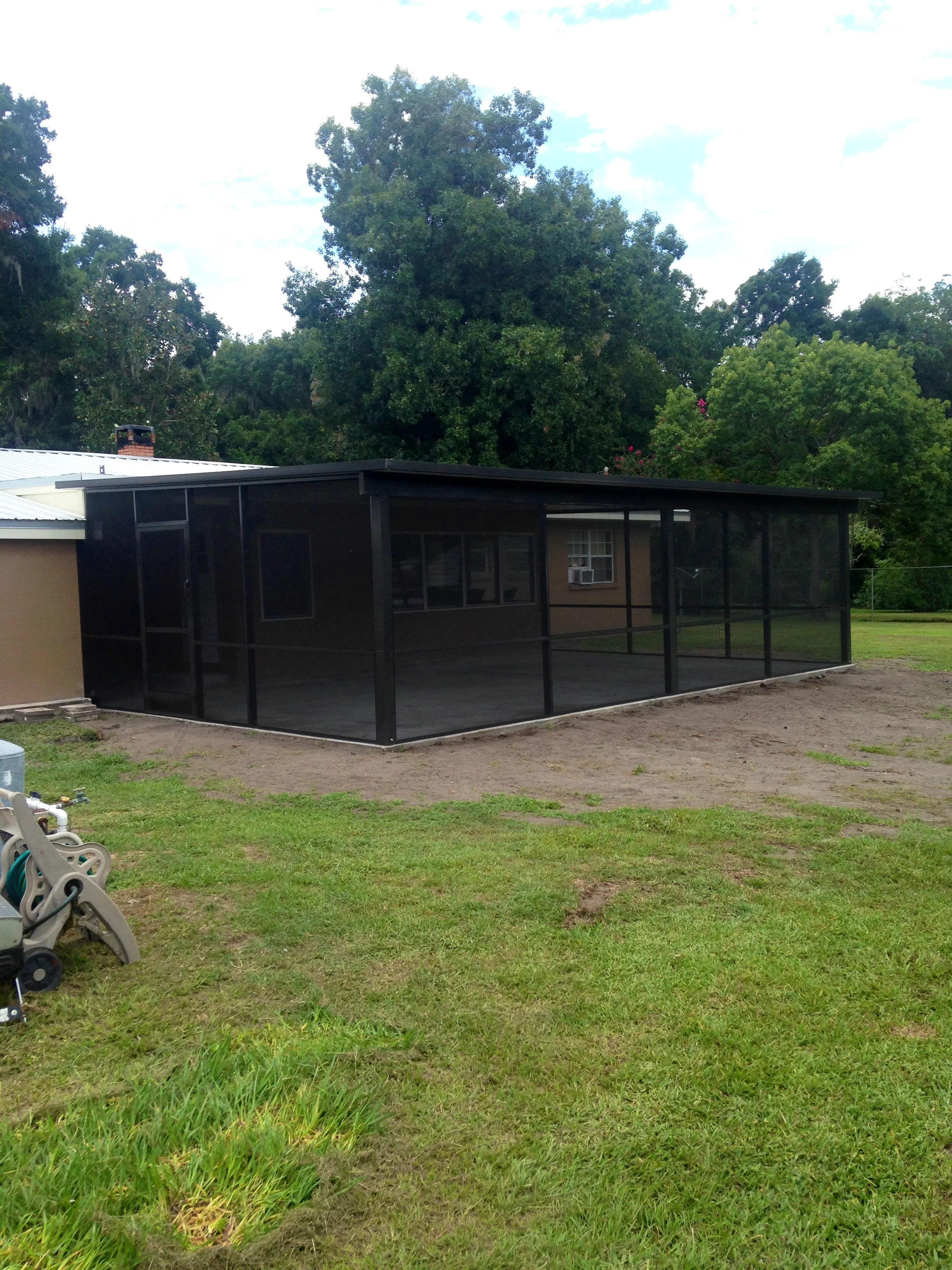 Black aluminum screen enclosure with glass doors and screen panels attached to residential structure
