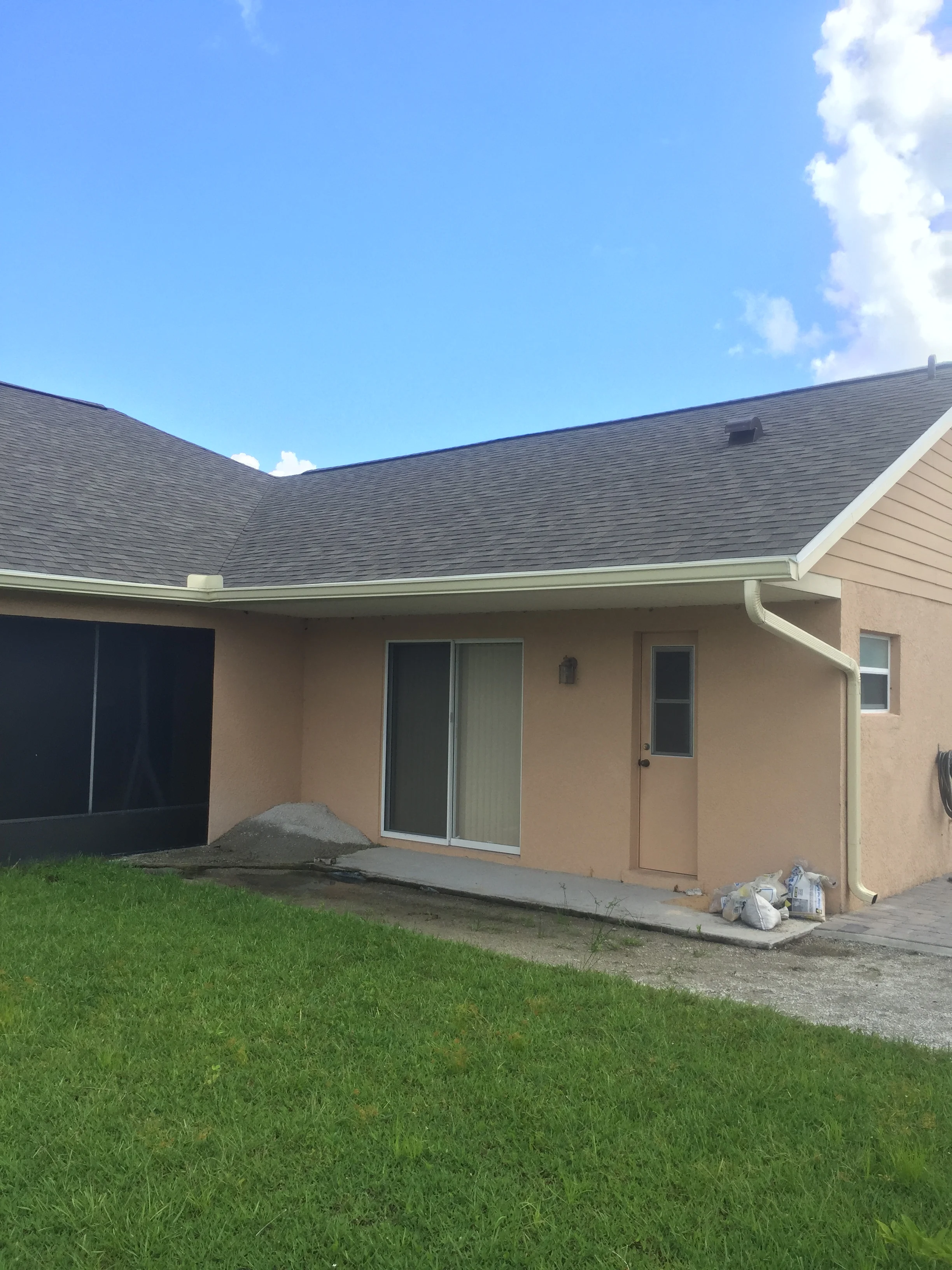 Concrete patio with stucco home, new gutters, and green lawn
