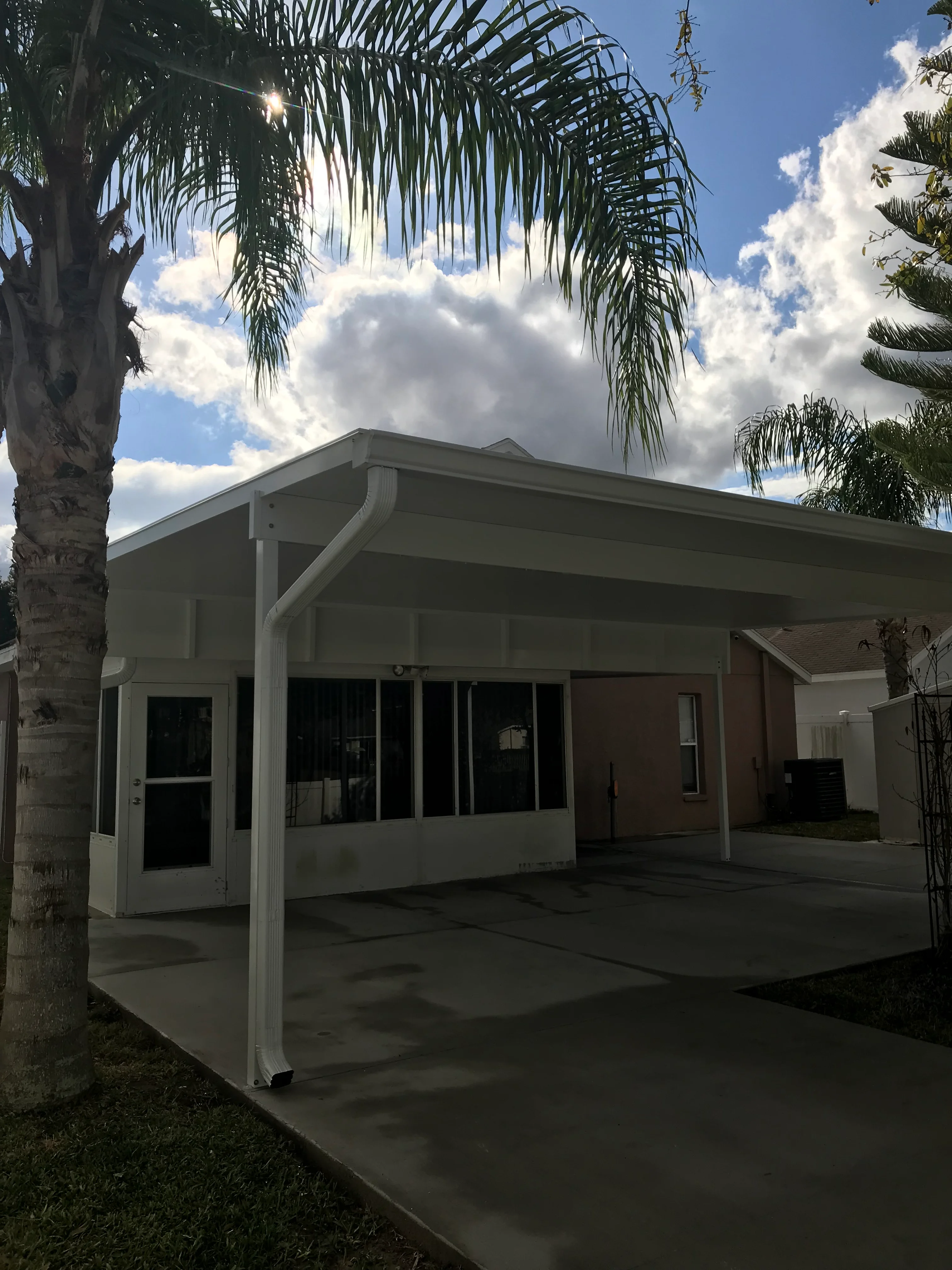 White aluminum covered patio with gabled roof, black-framed windows, and concrete pad