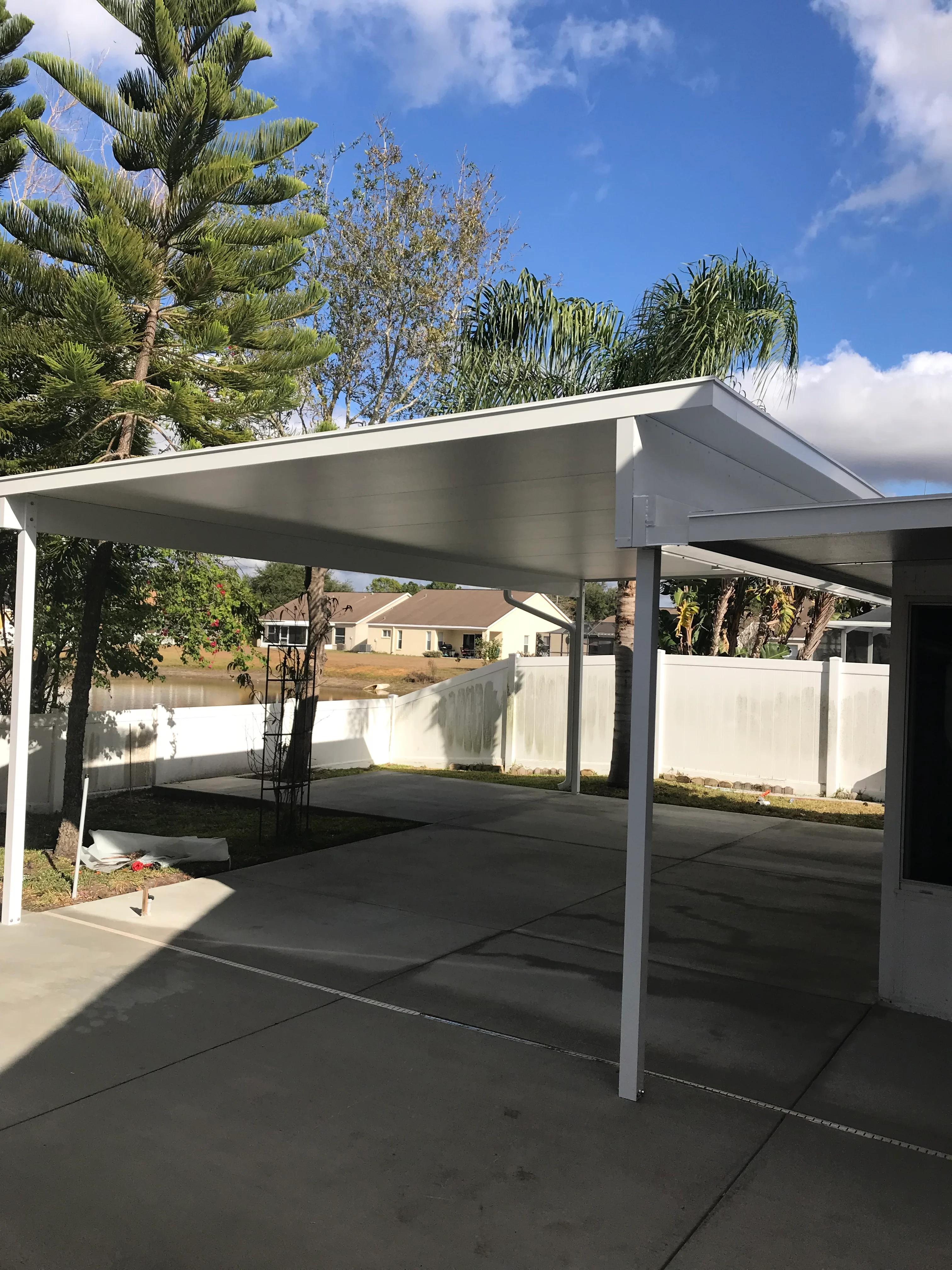 White aluminum carport with gable roof over concrete driveway, metal posts and beams