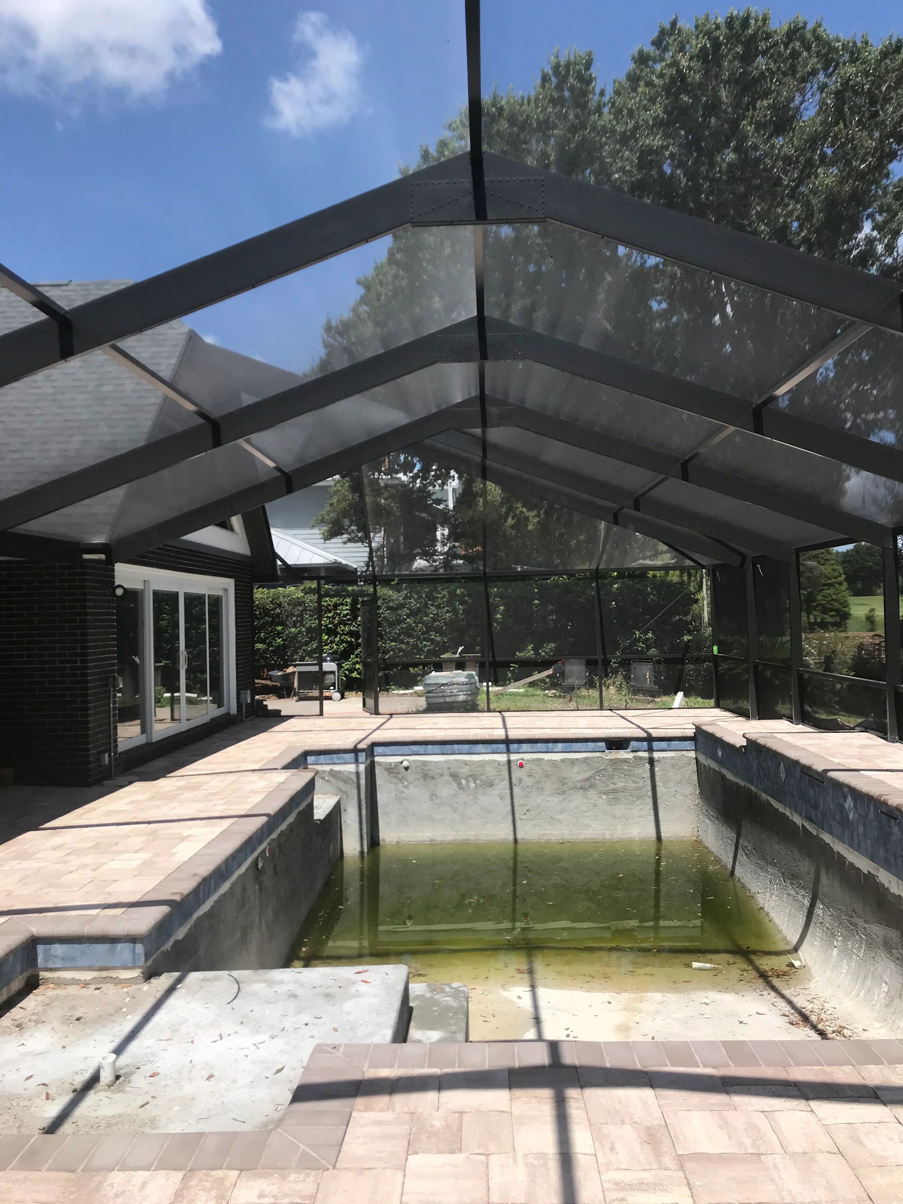 Black aluminum pool enclosure with polycarbonate roof and screened walls over in-ground pool with tan paver patio