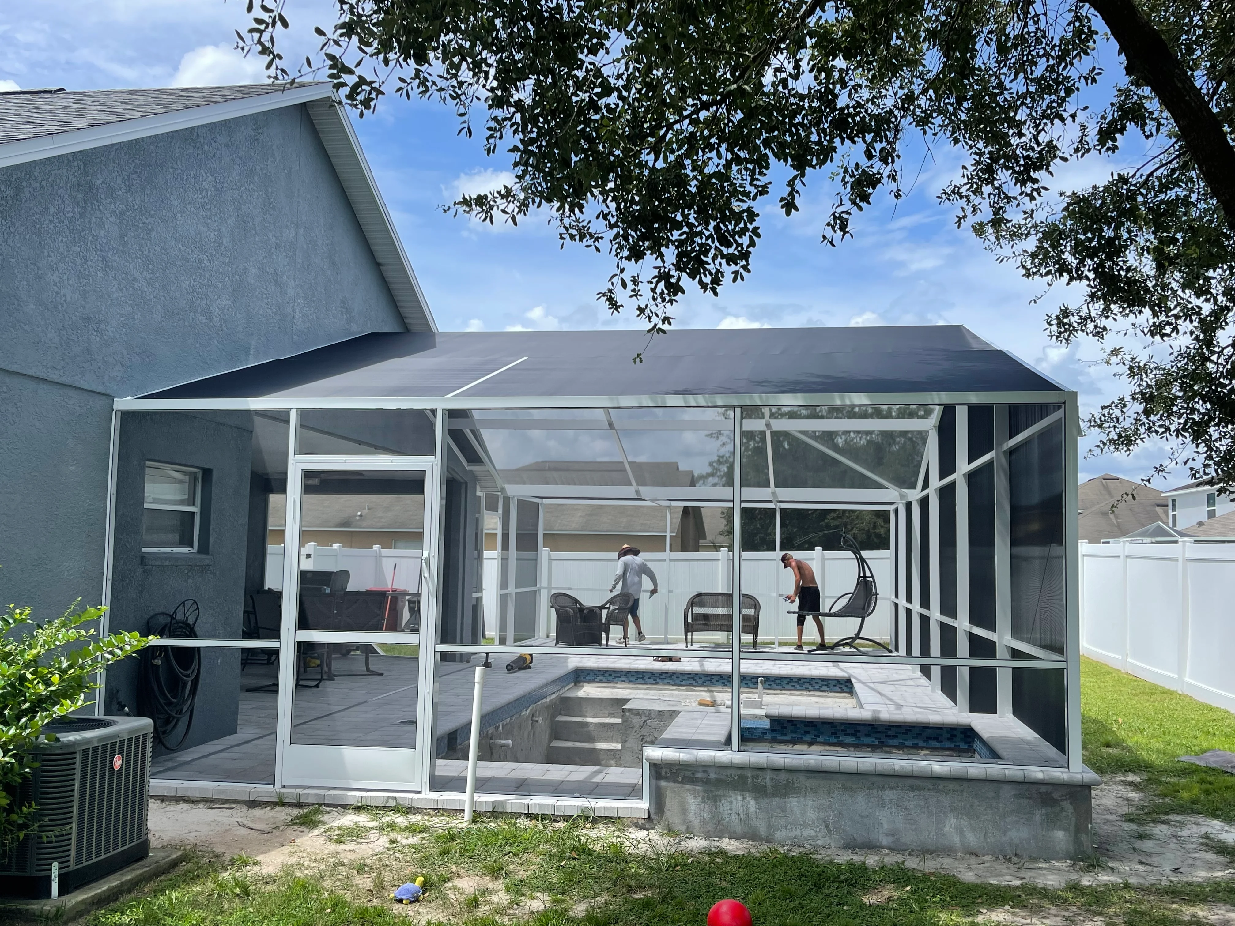 White aluminum screened patio with full-length windows and screening panels adjacent to concrete pool deck