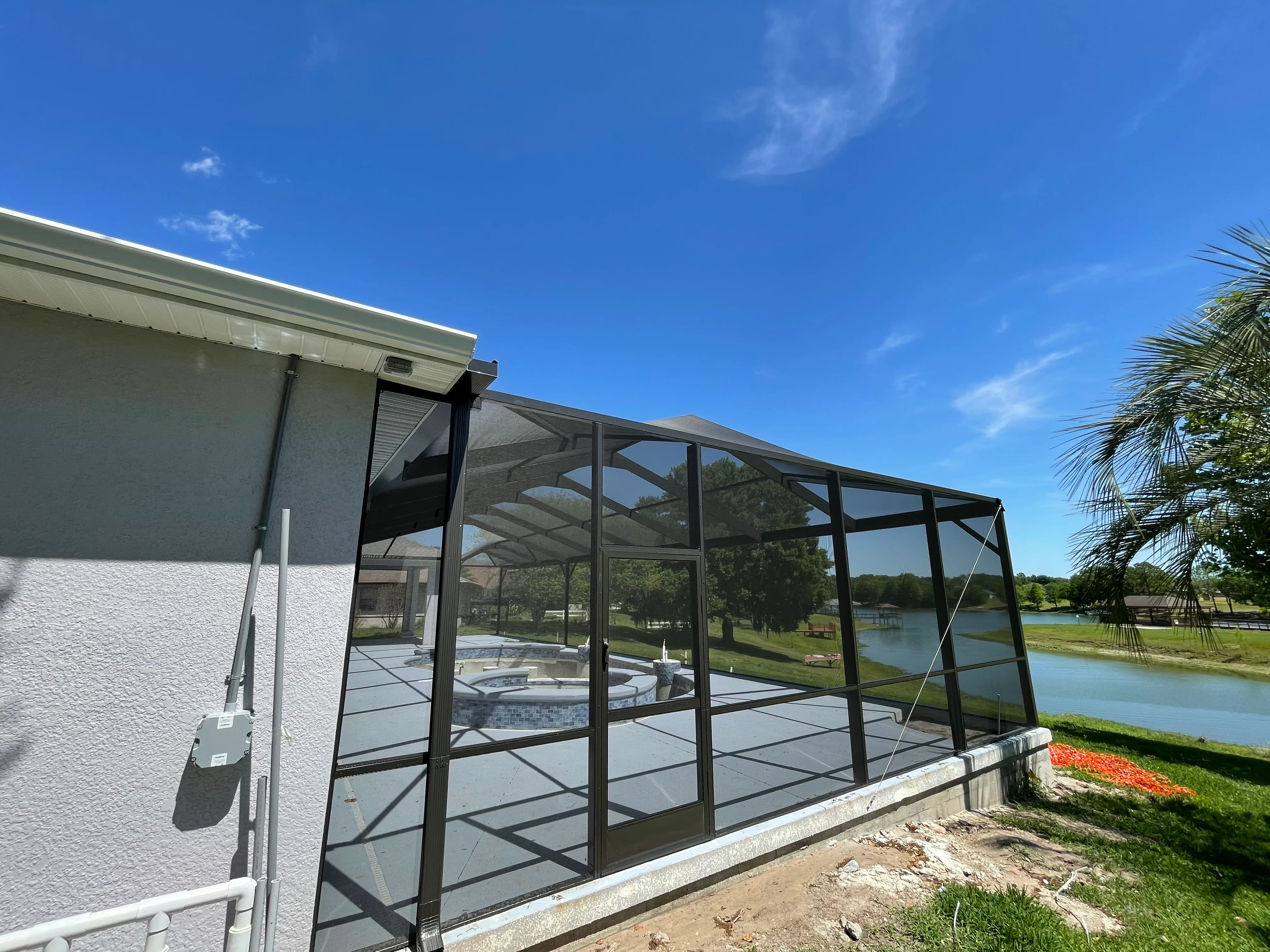 Black aluminum screened patio with gable roof, concrete foundation, and spa overlooking waterfront