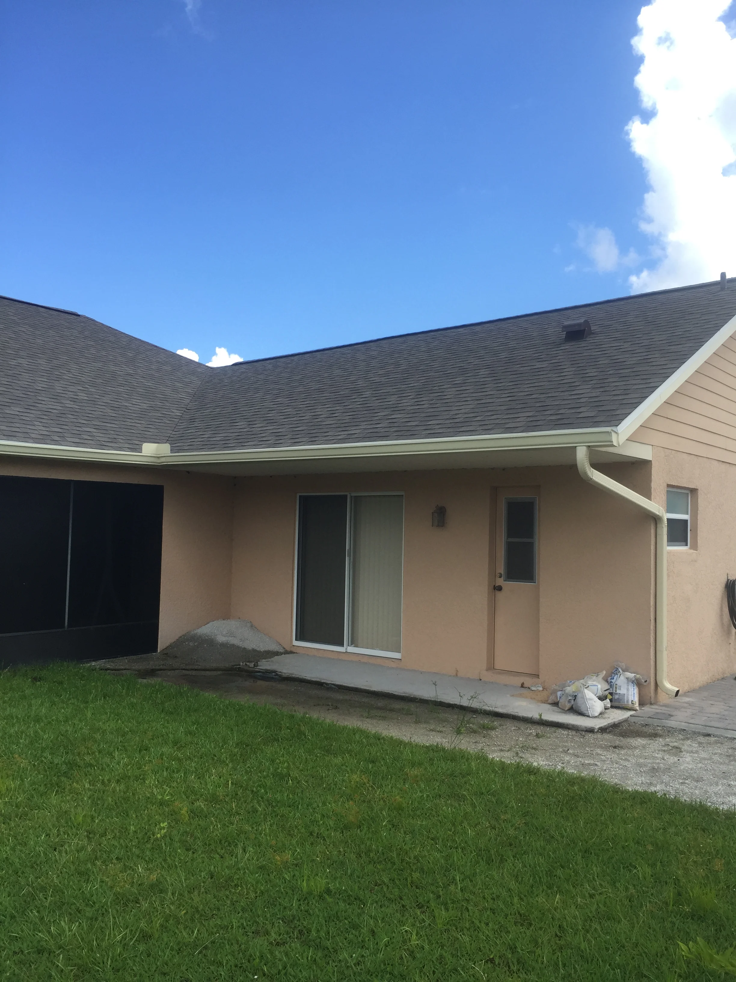Concrete patio with finished surface next to tan stucco home with dark roof