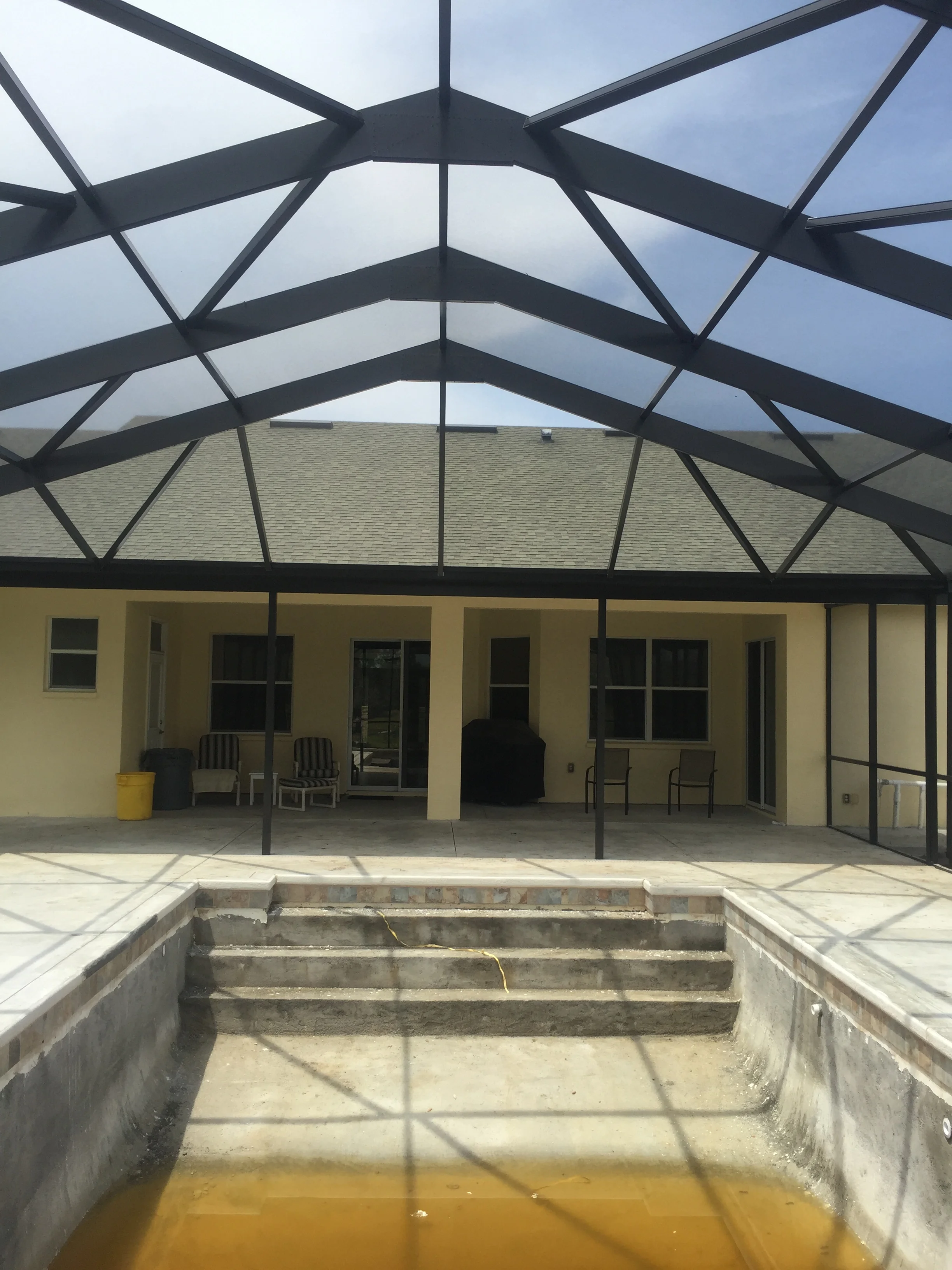 Black aluminum patio cover with arched beams, polycarbonate panels, and full screening over concrete patio area
