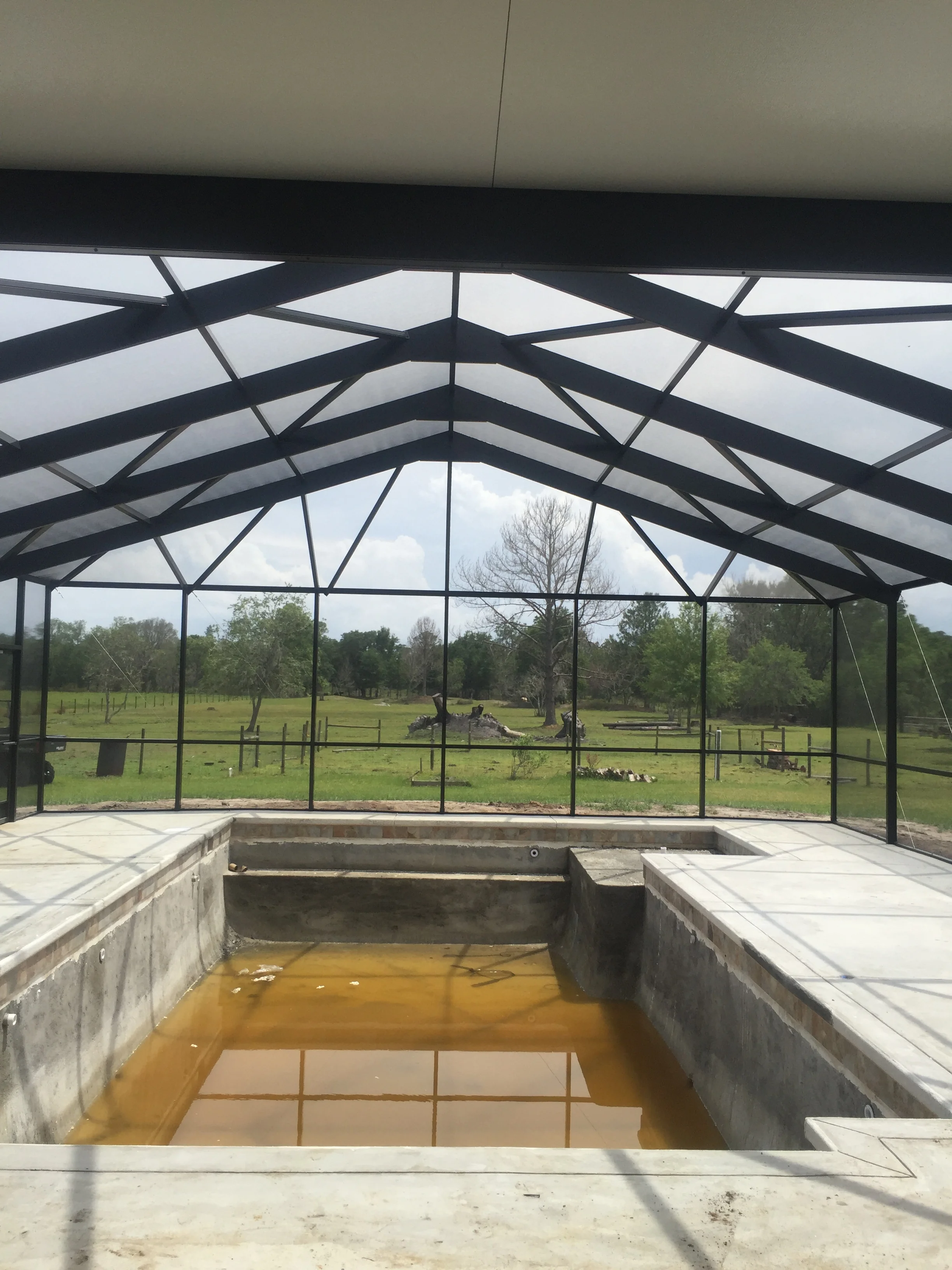 Black aluminum patio frame with polycarbonate roof panels and concrete foundation overlooking open grounds