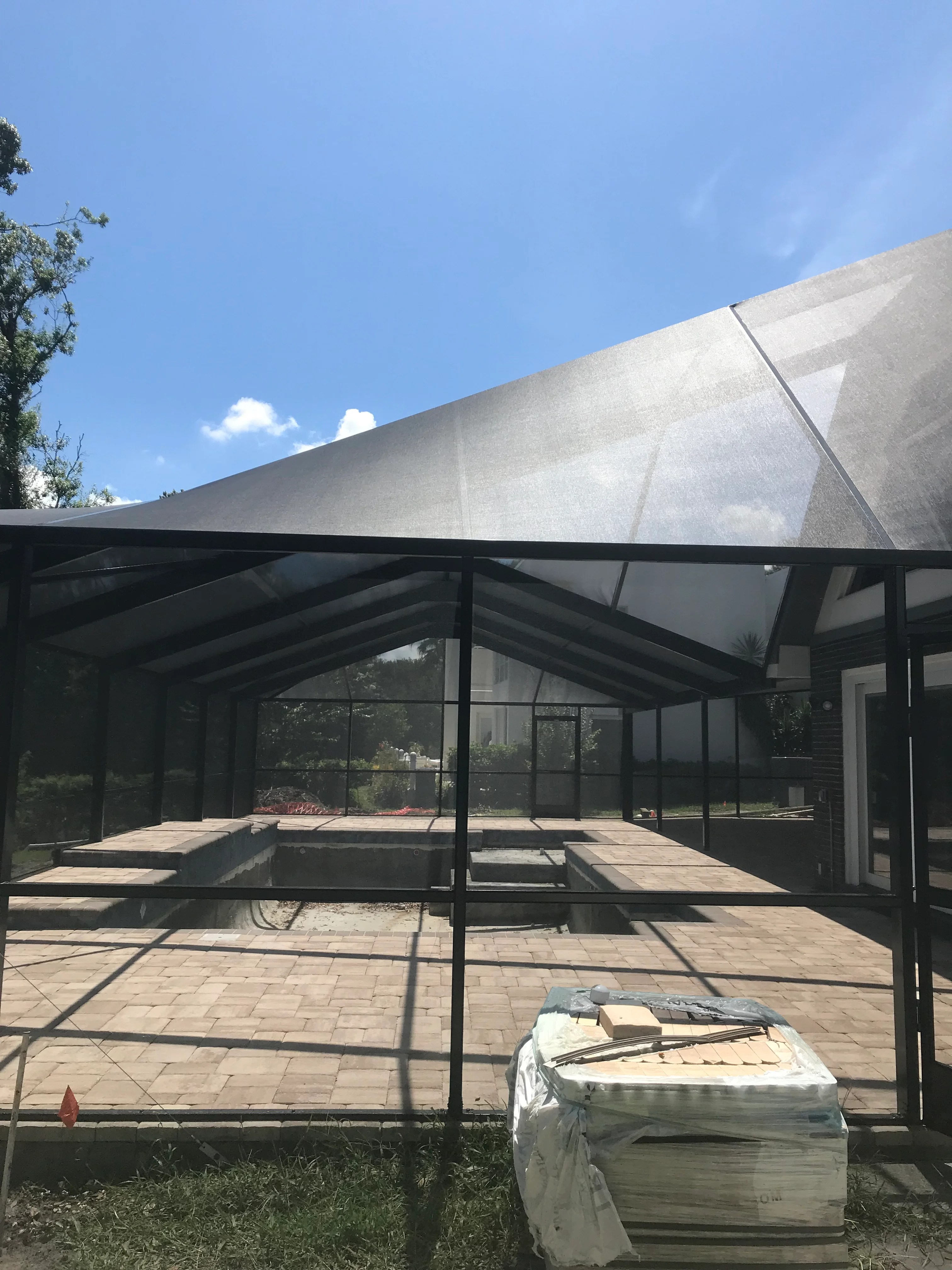 Screened patio with black aluminum frame, full screening, shade sail, and paver flooring
