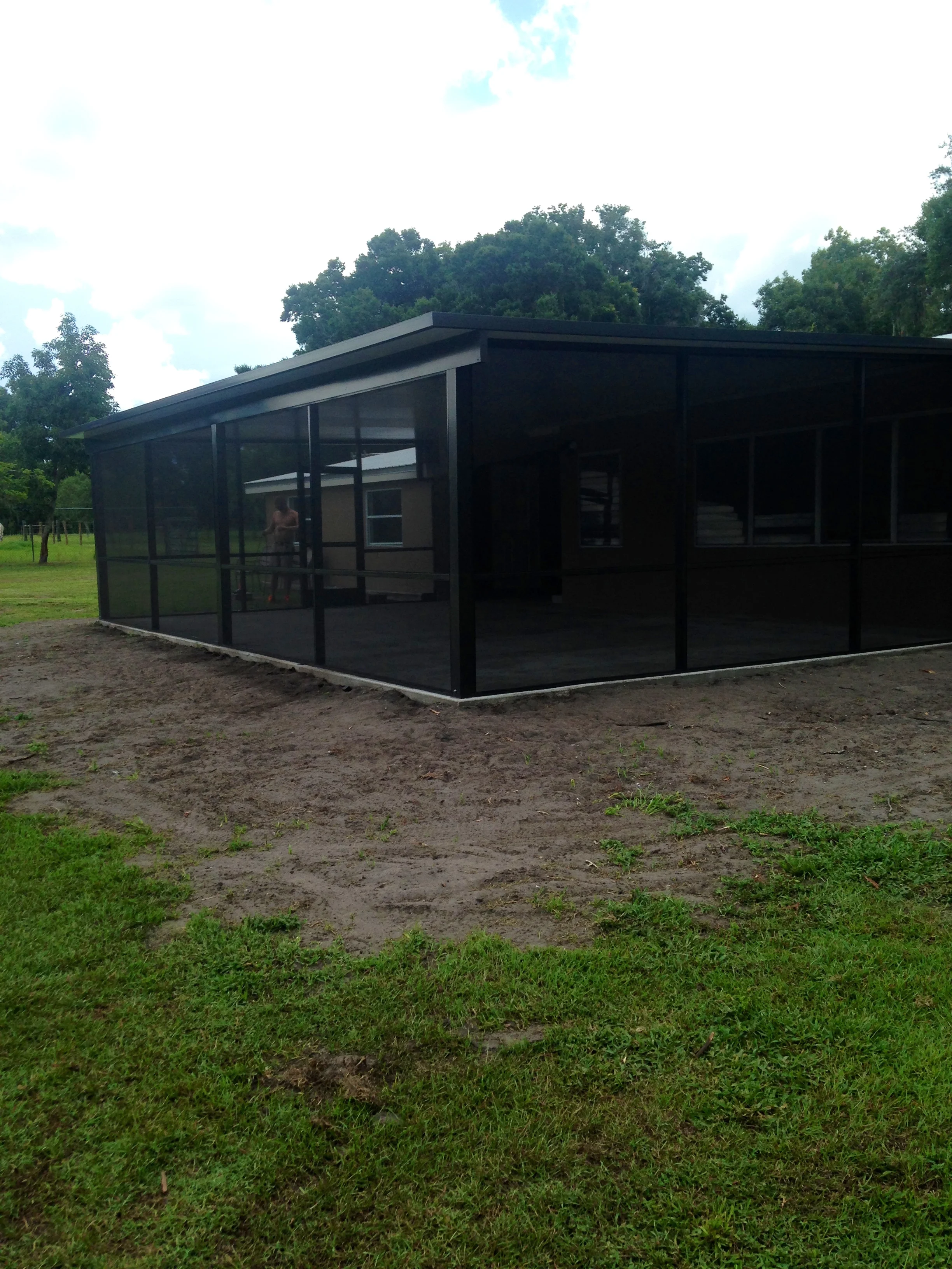 Black aluminum screened pavilion with glass panels and sloped roof on concrete pad
