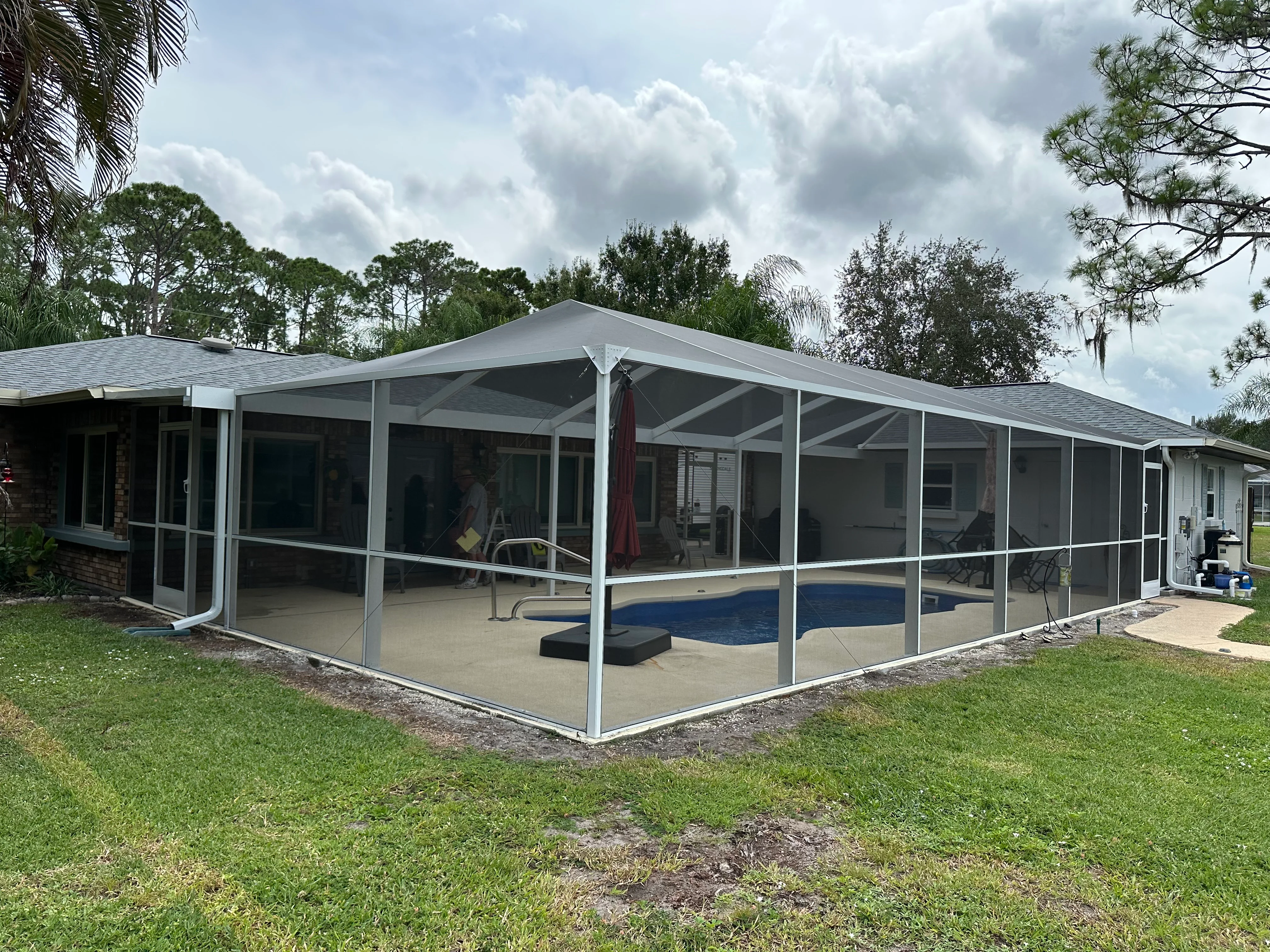 Aluminum pool enclosure with gable roof, white frame, and full screening around in-ground pool