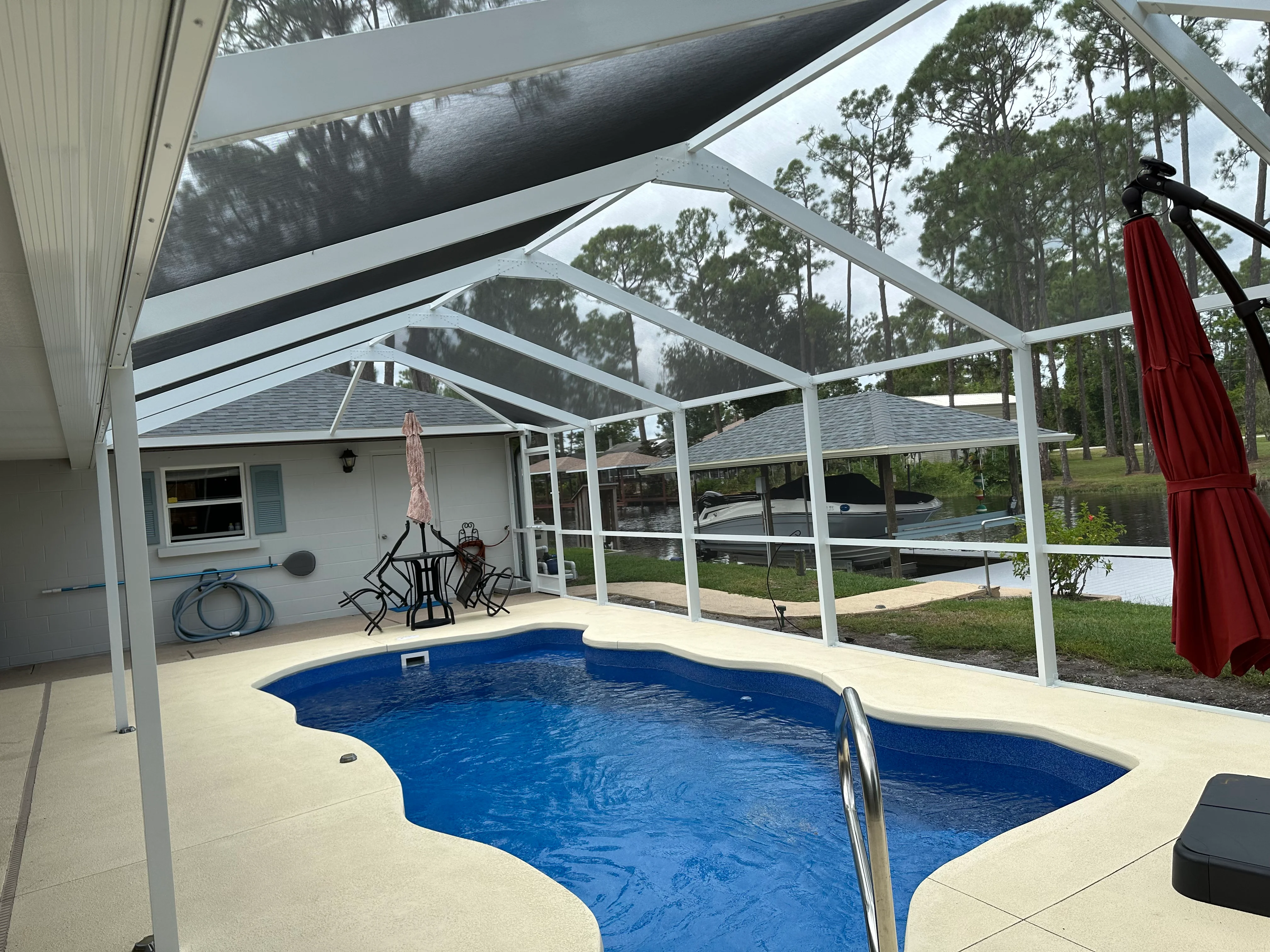 Aluminum pool enclosure with white frame, polycarbonate panels, and retractable shade sail over in-ground pool